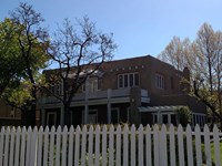 White picket fence in front of a two story adobe house with a white upstairs veranda.