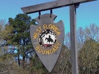 Wooden arrowhead shaped sign with yellow letters stating "West Florida Boundary" hangs from a post.