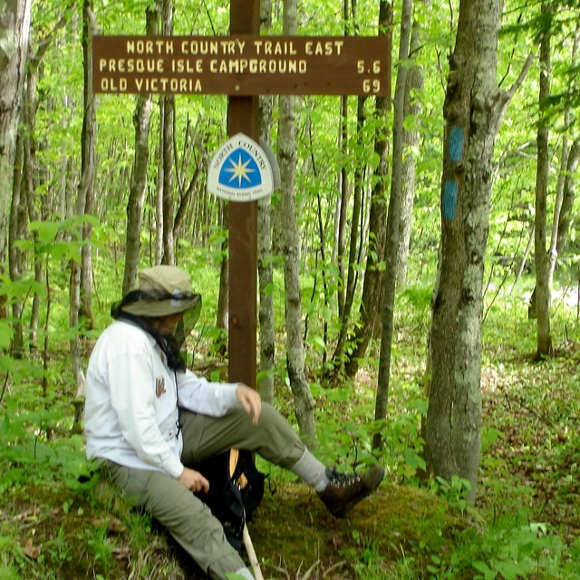Hiker sits on rock near North Country Trail sign. 