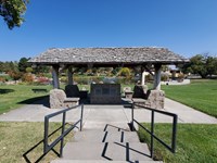 A shingle roof sits atop stone corner posts, surrounded by a grassy lawn
