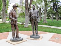 Bronze statues of two men stand on a concrete pad