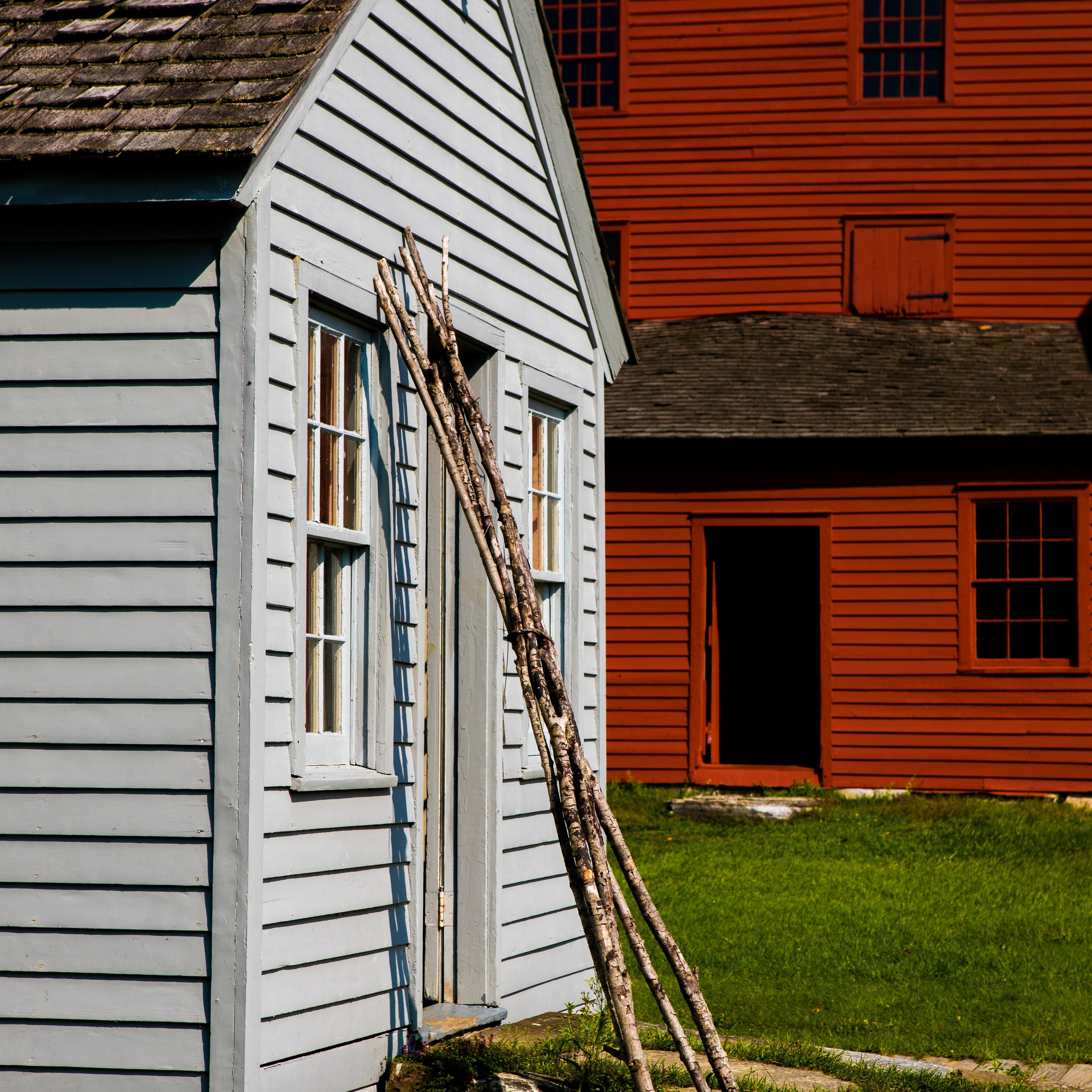 large branches resting against a one story clapboard building, red barn in background