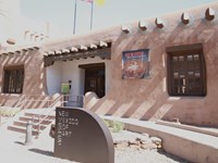 A large pink adobe building with large trees in front.
