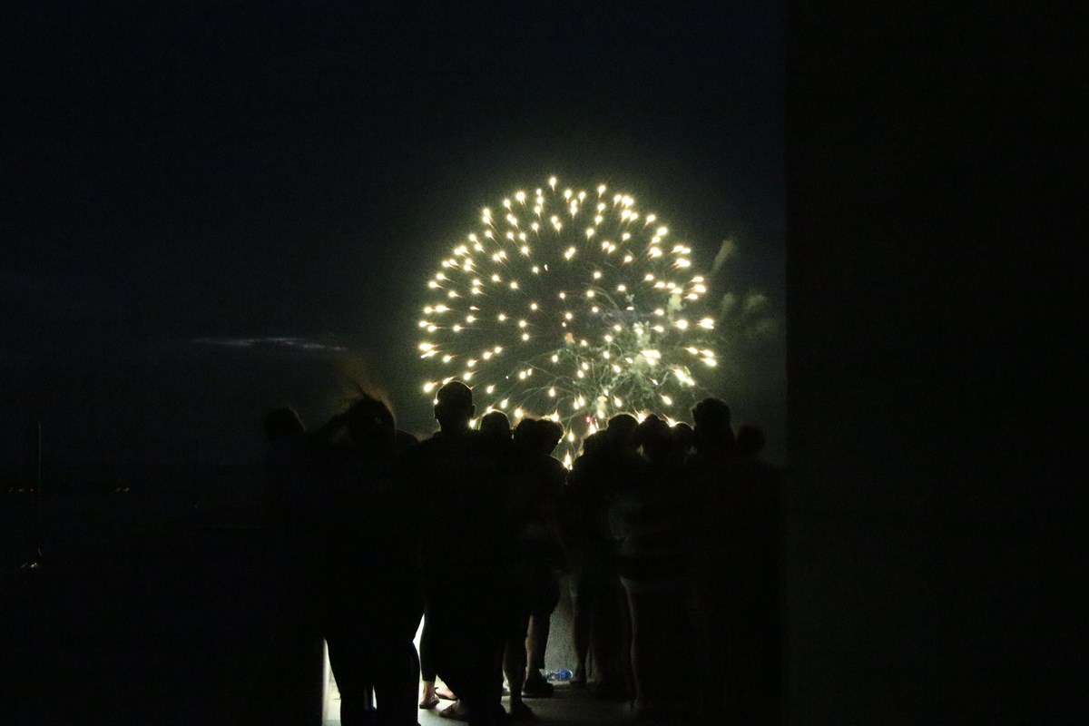 Fireworks bursting over a crowd of visitors standing in the dark on the Monument's observation deck.
