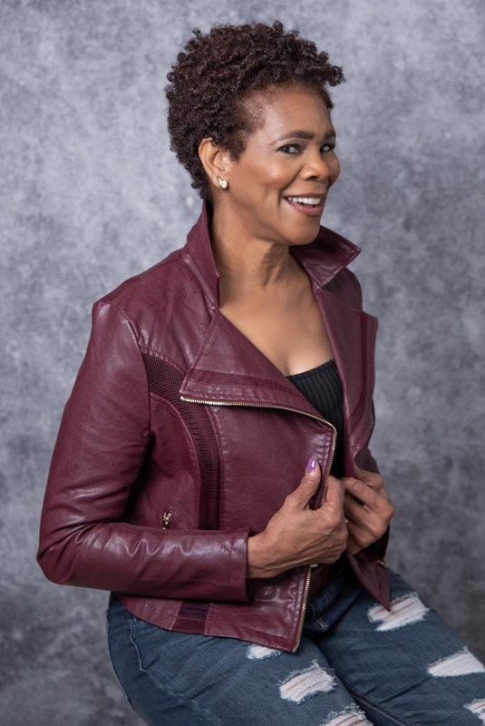 Seated African American woman, smiling, wearing burgundy jacket and jeans