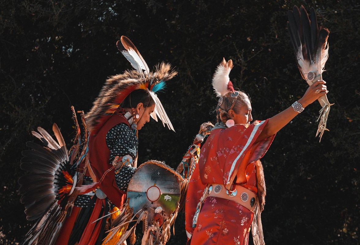 Two individuals dressed in native regalia performing traditional dance.