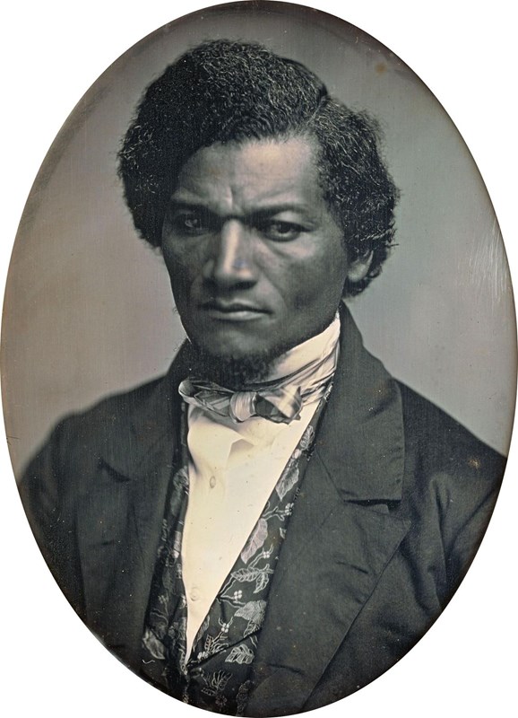 A young Frederick Douglass sits for a portrait wearing a suit jacket, shirt, vest, and tie