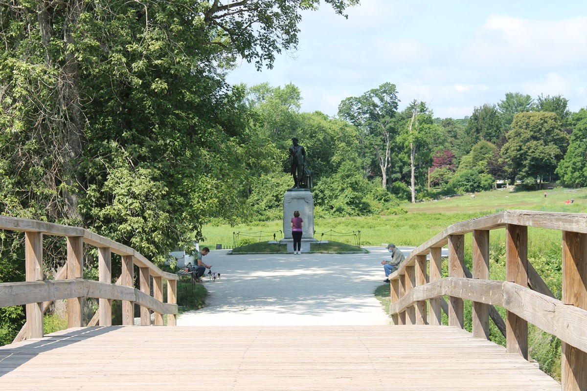 Standing in the middle of a wooden bridge with railings on either side, looking toward a statue.