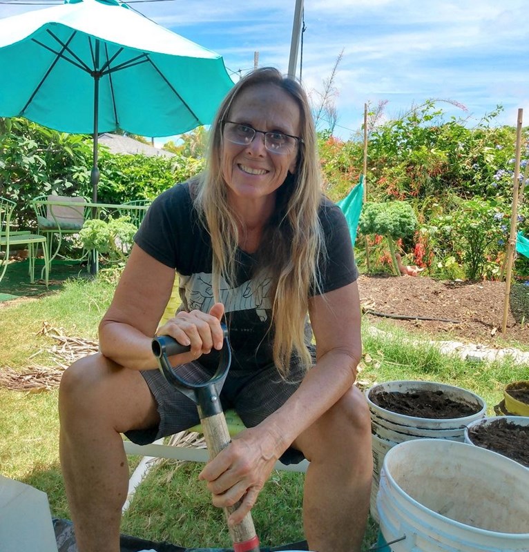 A woman holding a shovel leans over a bucket of what might be dirt