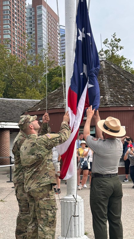Uniformed Park Rangers and Soldiers raise an American flag as the public looks on.
