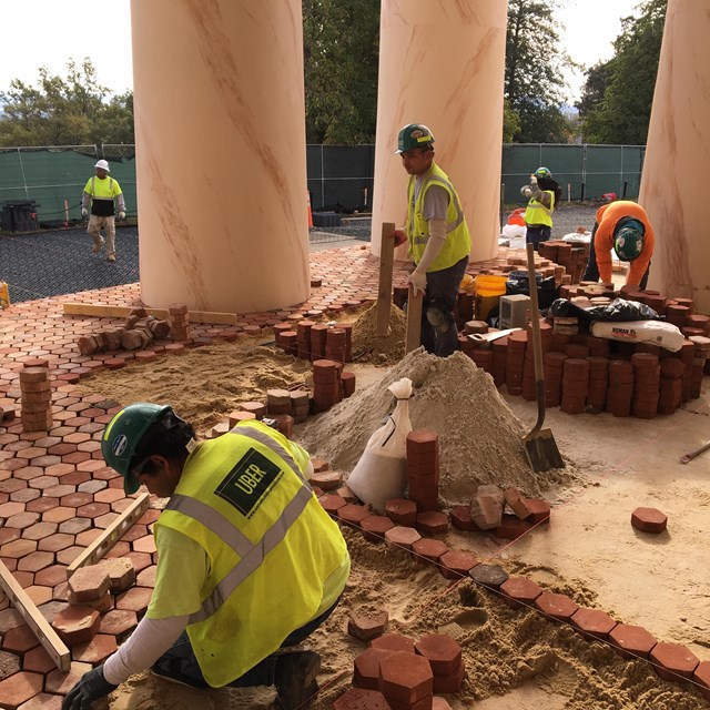 Construction workers wearing hard hats remove hexagonal tiles from a porch floor.