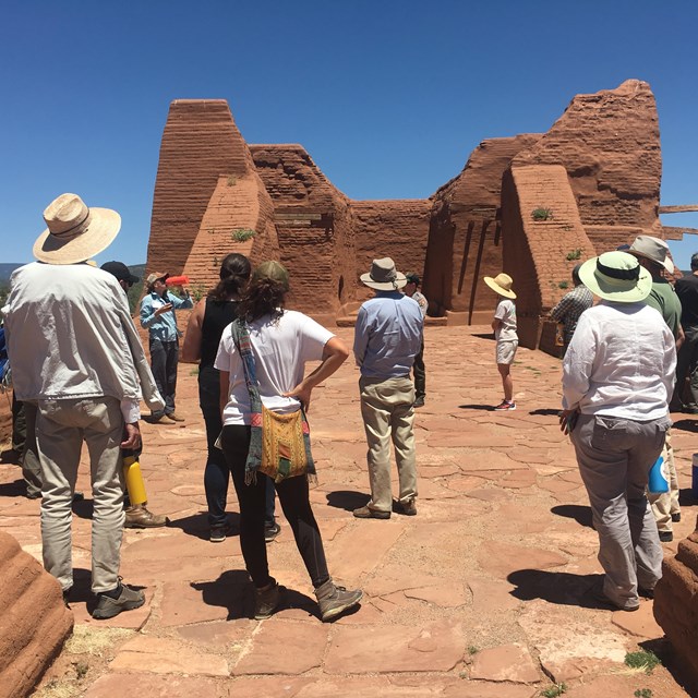 A group of people in an adobe structure listen to an instructor.