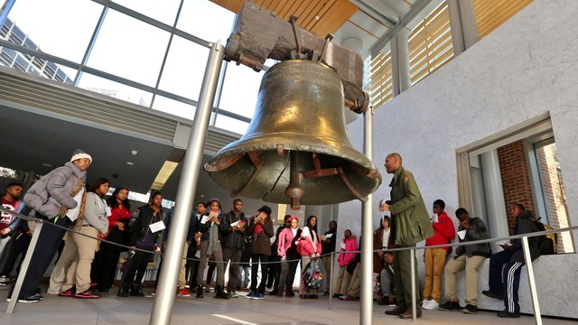 A group of students and a park ranger stand around the Liberty Bell.