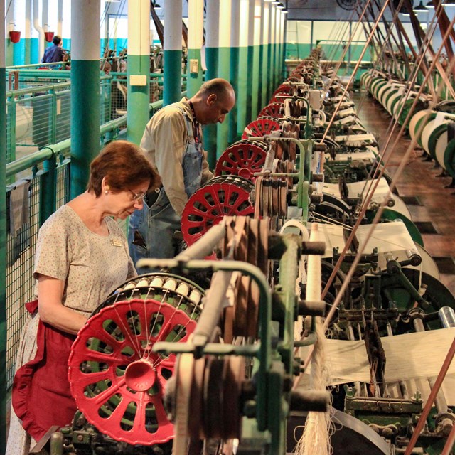 A man and a woman stand working at a row of identical machines