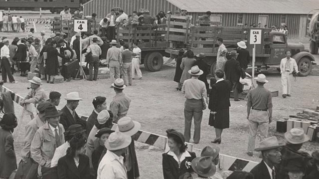 people standing in line next to a barricade as other people are loaded into the back of open trucks