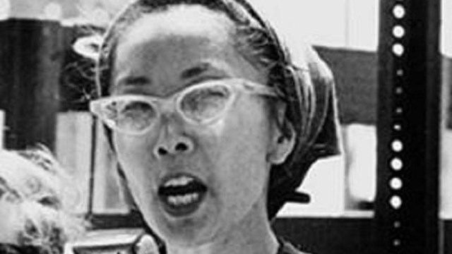 Black and white photo of Yuri Kochiyama with a speaker looking at the camera.