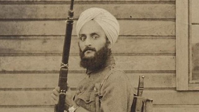 Sepia photo of Bhagat Singh Thind during his Army service, holding military arms, looks to camera.