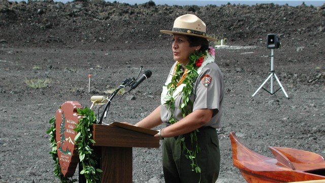 A woman in the National Park Service uniform stands at a podium.