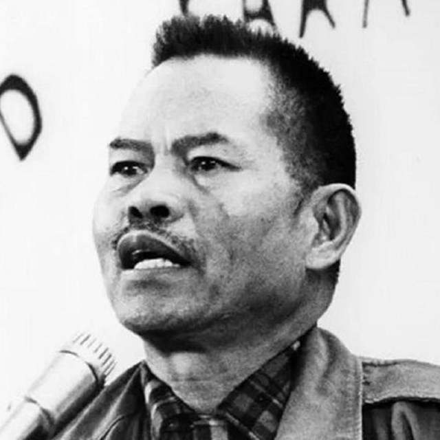 Black and white photo of Larry Itliong at a podium looking at the camera.