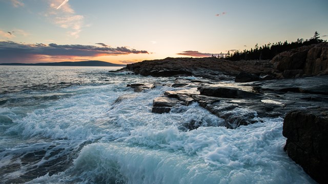 Waves crash against rocky coastline at sunset