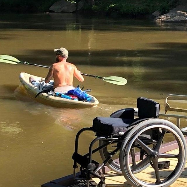 Man kayaking on a river with his wheelchair on the dock in the foreground.  