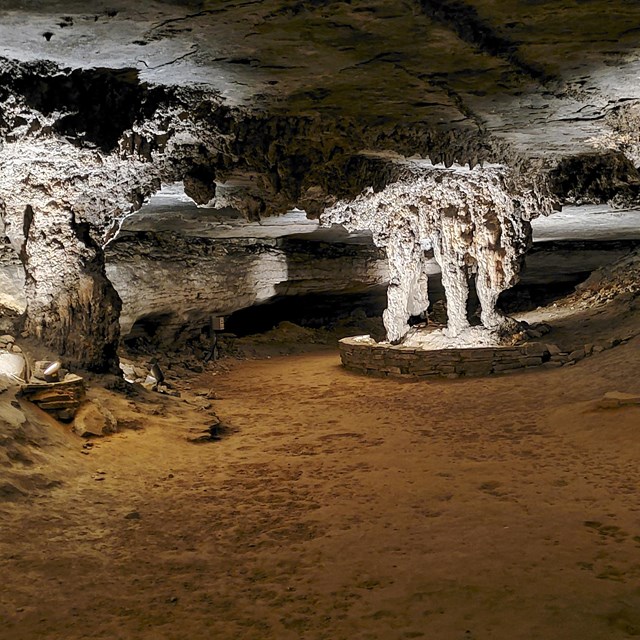 grey pillars of stalagmites in a hikeable cave room.  Room is are lit by artificial light.  
