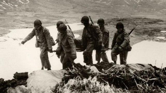 a historic scene of five soldiers carrying a litter with a person on it through mountainous terrain.