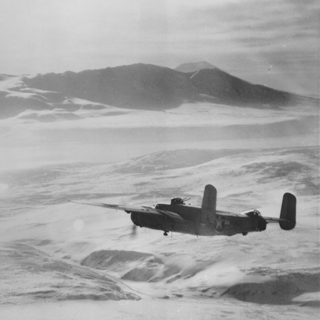 a historic scene of a plan flying high over snow-covered mountain peaks.