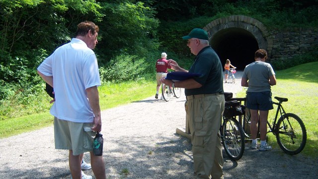 A volunteer talking with visitors near a railroad tunnel.
