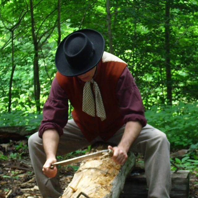 Costumed park ranger demonstrates use of a draw knife.