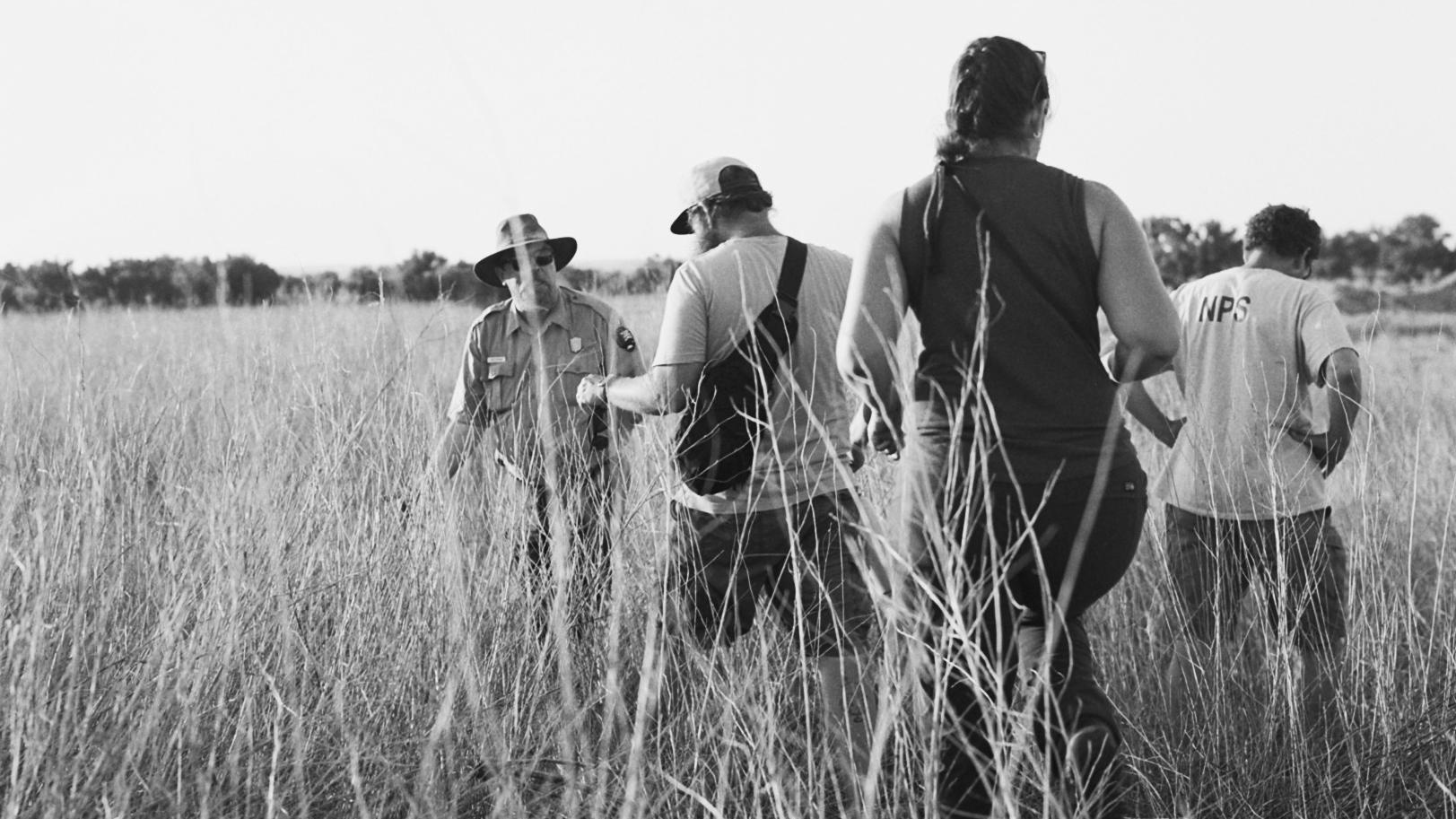 Three people following a ranger through a field.