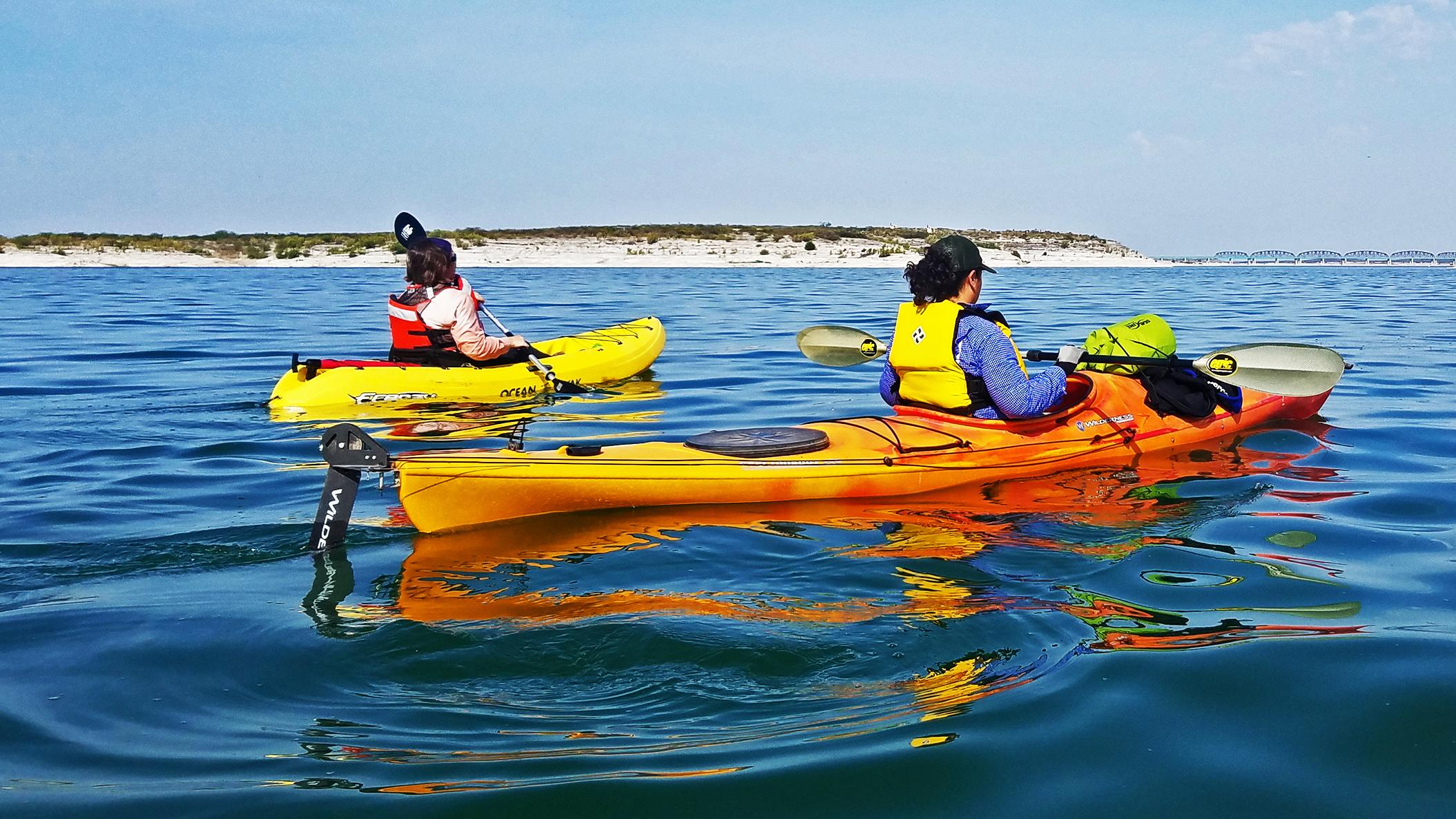 Two single-person, sit-down-in, touring kayaks on calm, crystal blue reservoir