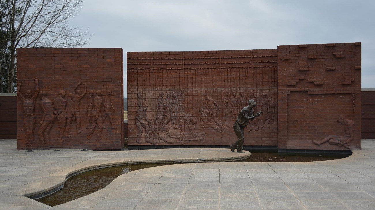 A courtyard with a large wall sculpture and statue of prisoners of war