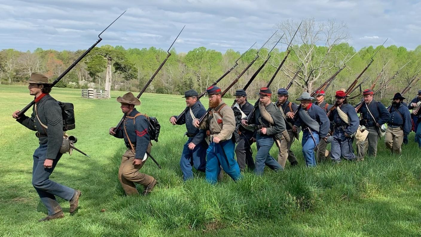Civil war era dressed soldiers march through a grassy field