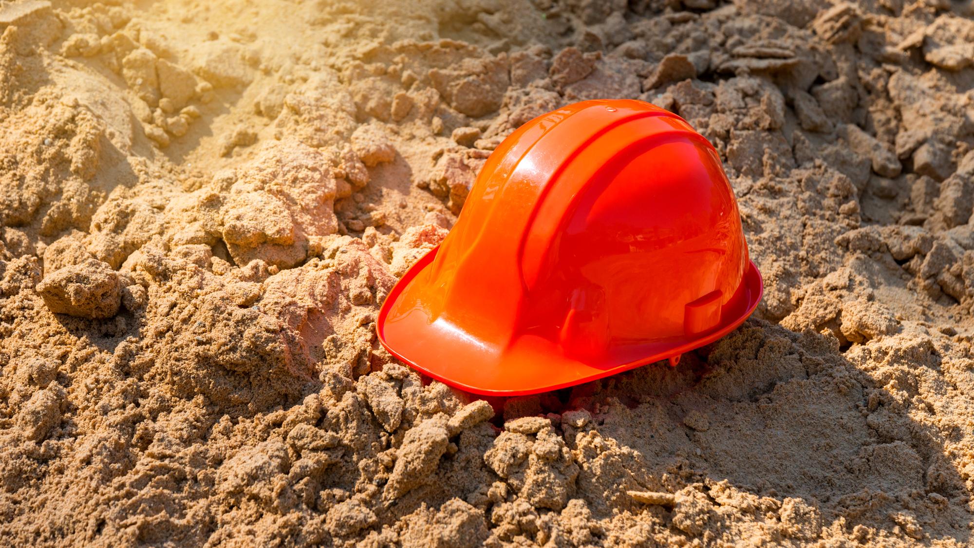 Photograph of orange hard hat in sand. 