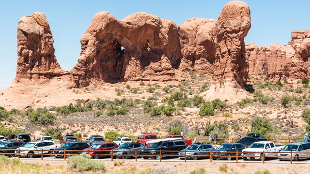 cars crowded into parking spaces below towering sandstone features