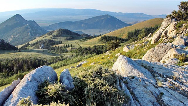 Panoramic shot of light-colored rocks, green slopes, and pointed peaks.