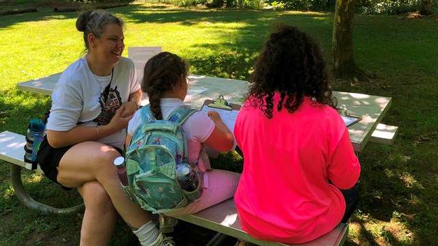 A parent and children sitting at a picnic table enjoying a science activity.