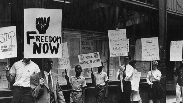 Black and white photograph of protesters with different handwritten picket signs