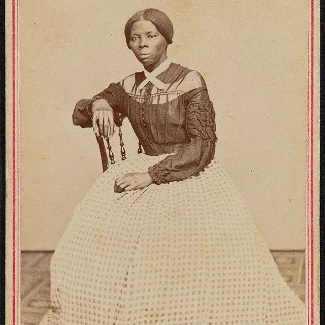 Young African American woman seated in dark top and light colored checkered skirt