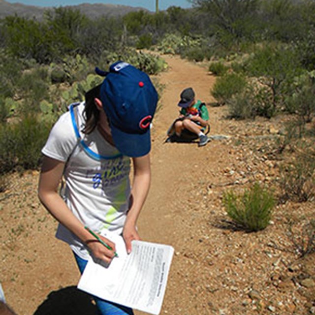 Photo of Talia on a dirt trail making notes