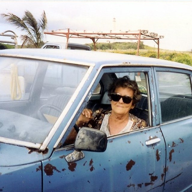 Woman smiles sitting in blue car with rust spots