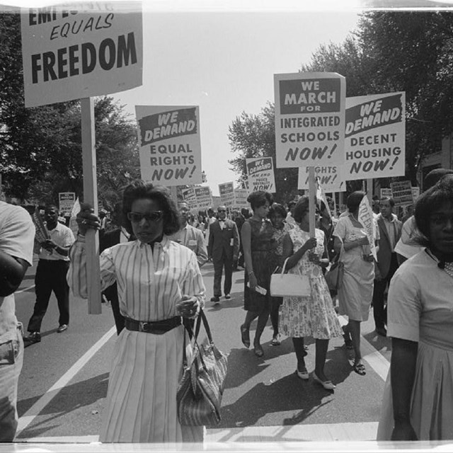 Women in dresses march holding picket signs