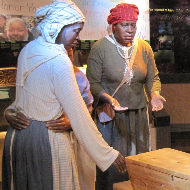 Statues of enslaved people around a small coffin