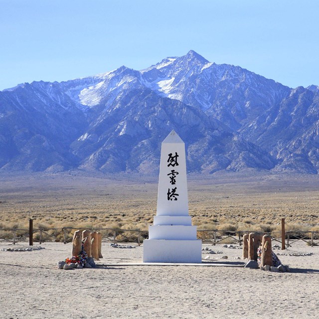 A white obelisk with Japanese characters stands against a backdrop of mountains