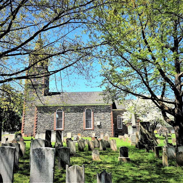 A stone church surrounded by trees with a graveyard in the foreground