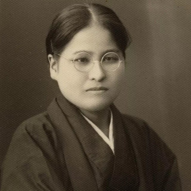 An East Asian woman in glasses wearing dark clothing