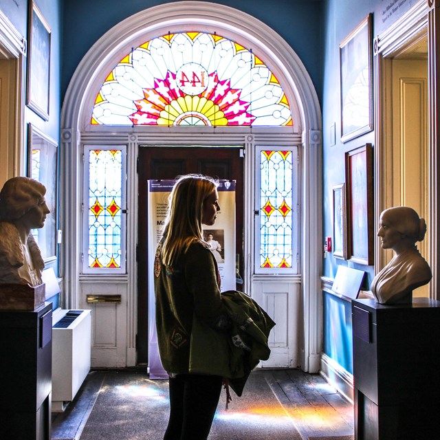 White woman standing in a hallway looking at a bust and painting