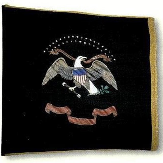 Dark blue flag with shield and eagle in middle and gold lettering on red scroll