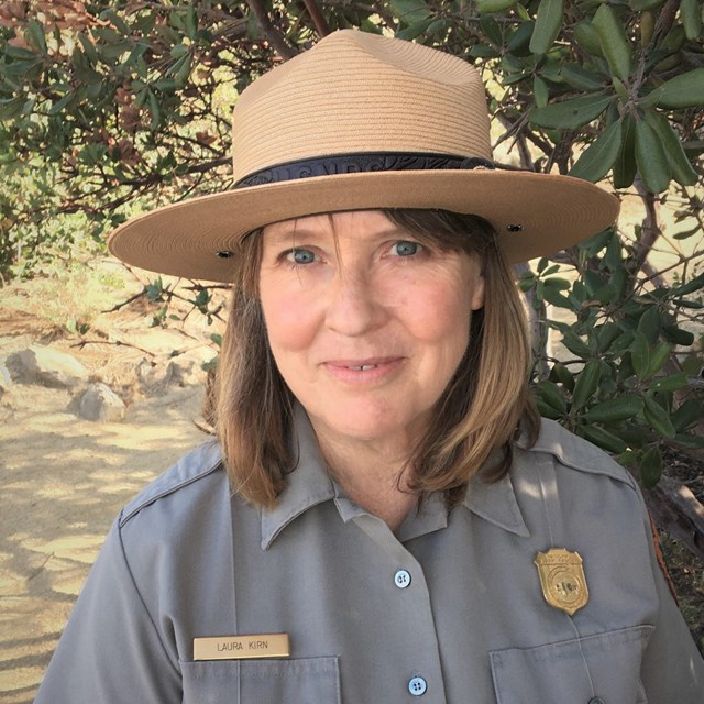 Blonde woman in flathat and NPS uniform smiles at the camera